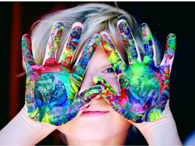 autistic child holding hands up with colorfully painted hands